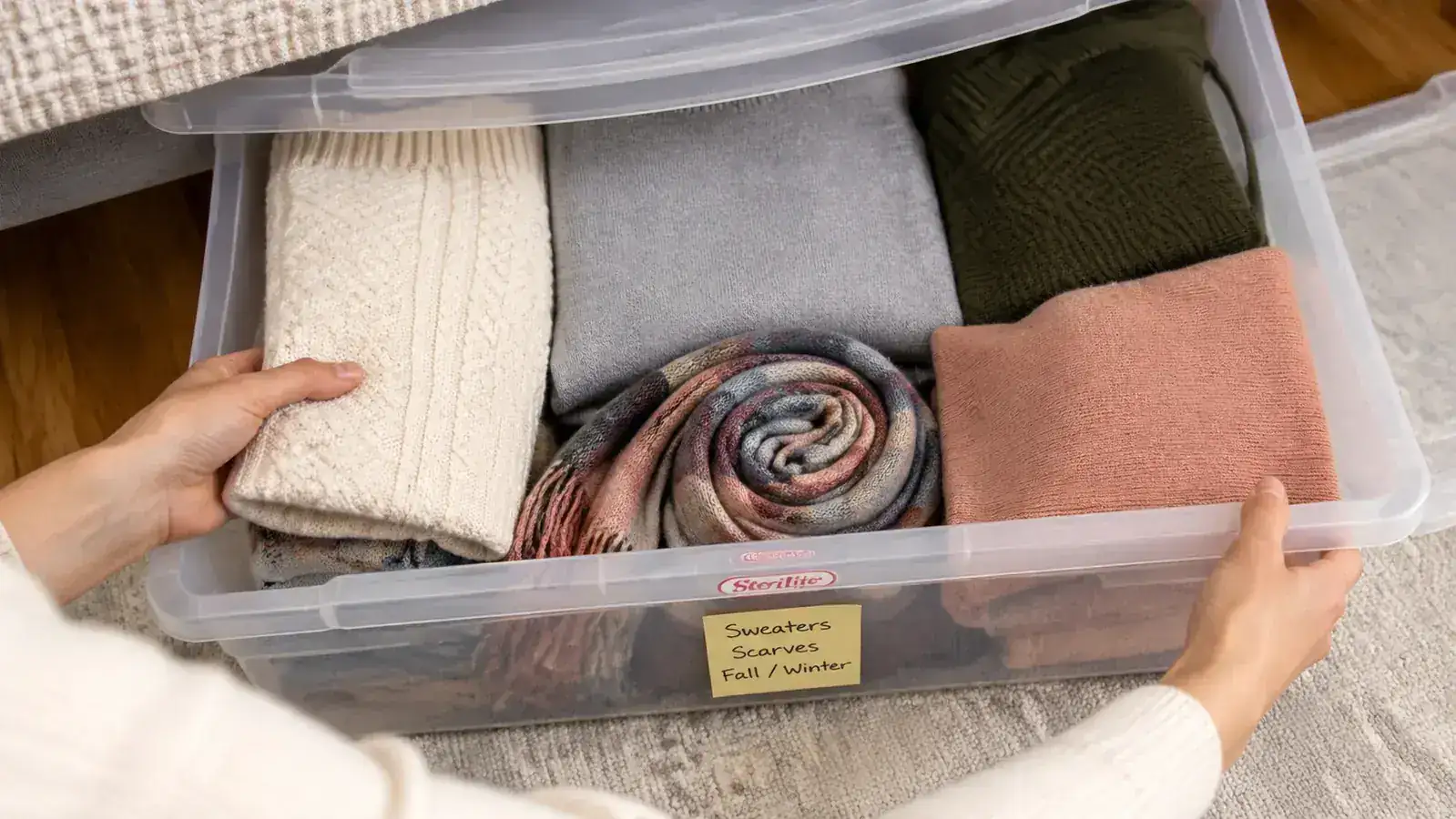 Open Sterilite under-bed bin filled with neatly folded sweaters and a visible divider between winter and summer items