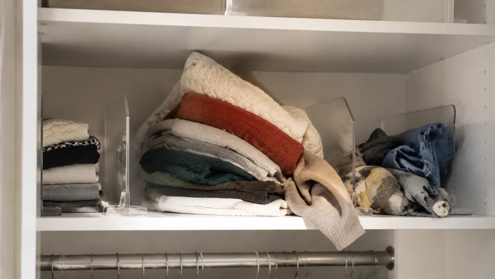Closet shelf with acrylic dividers showing a sweater pile leaning sideways and slipping past the divider